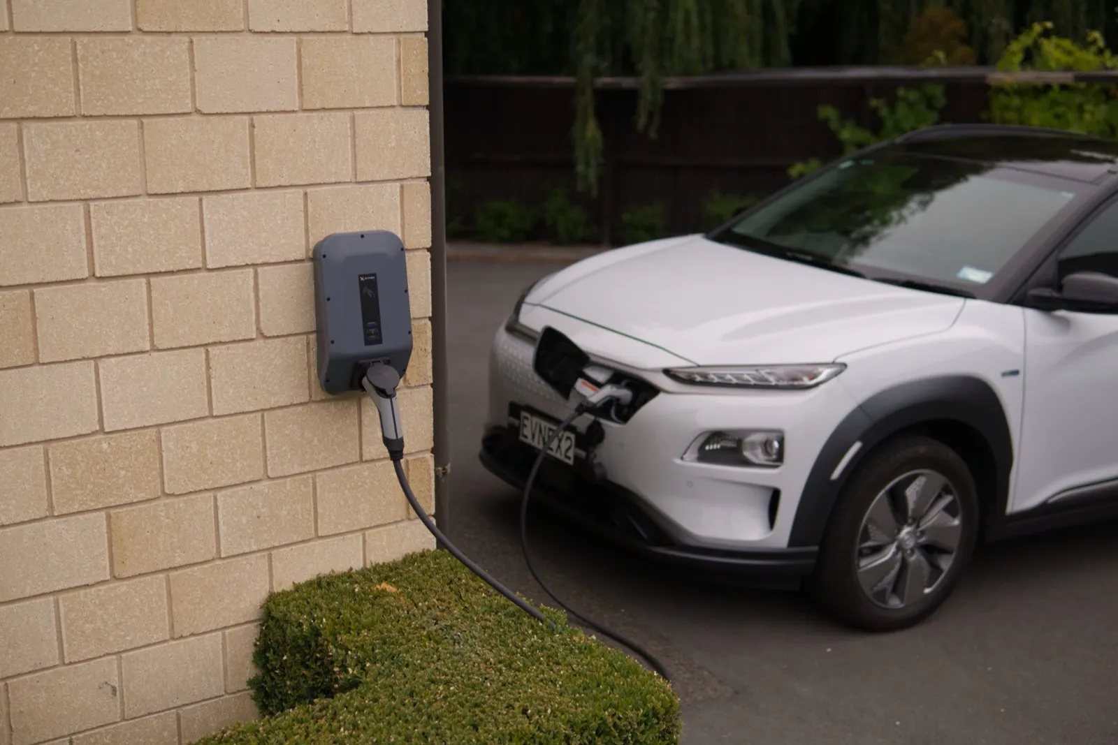 Wallbox an einer Hauswand, angeschlossen an ein weißes Elektroauto in der Einfahrt