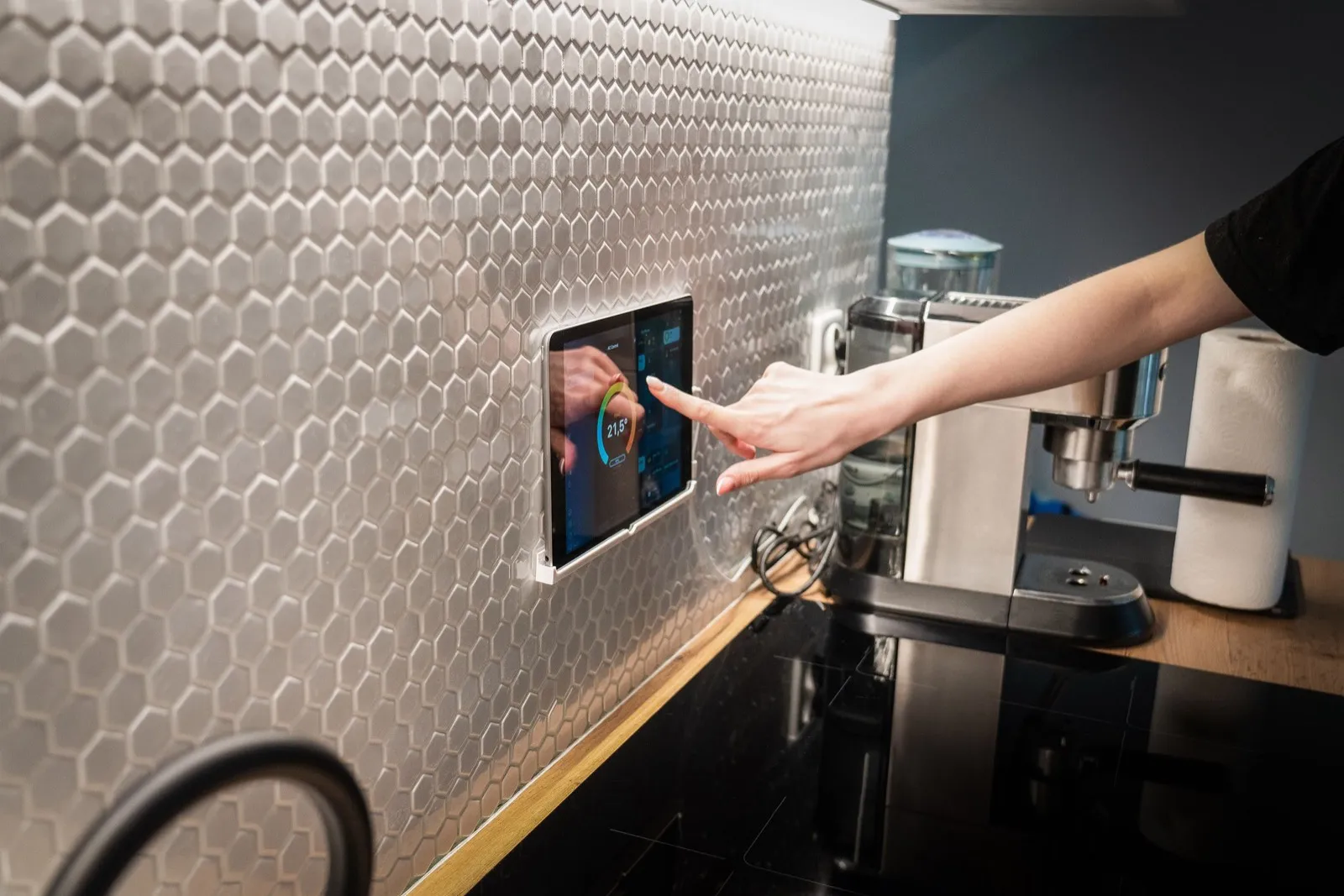Hand bedient ein an der Küchenwand montiertes Steuerdisplay für die Haustechnik