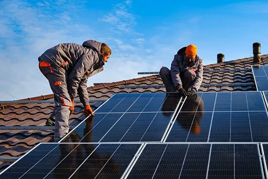 Zwei Monteure befestigen Solarmodule auf einem Ziegeldach