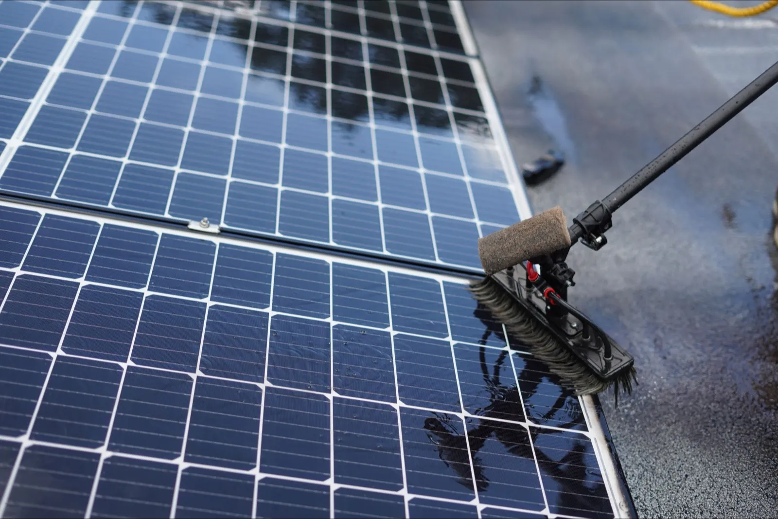 Solarmodul wird mit einer Wasserbürste auf Teleskopstange gereinigt