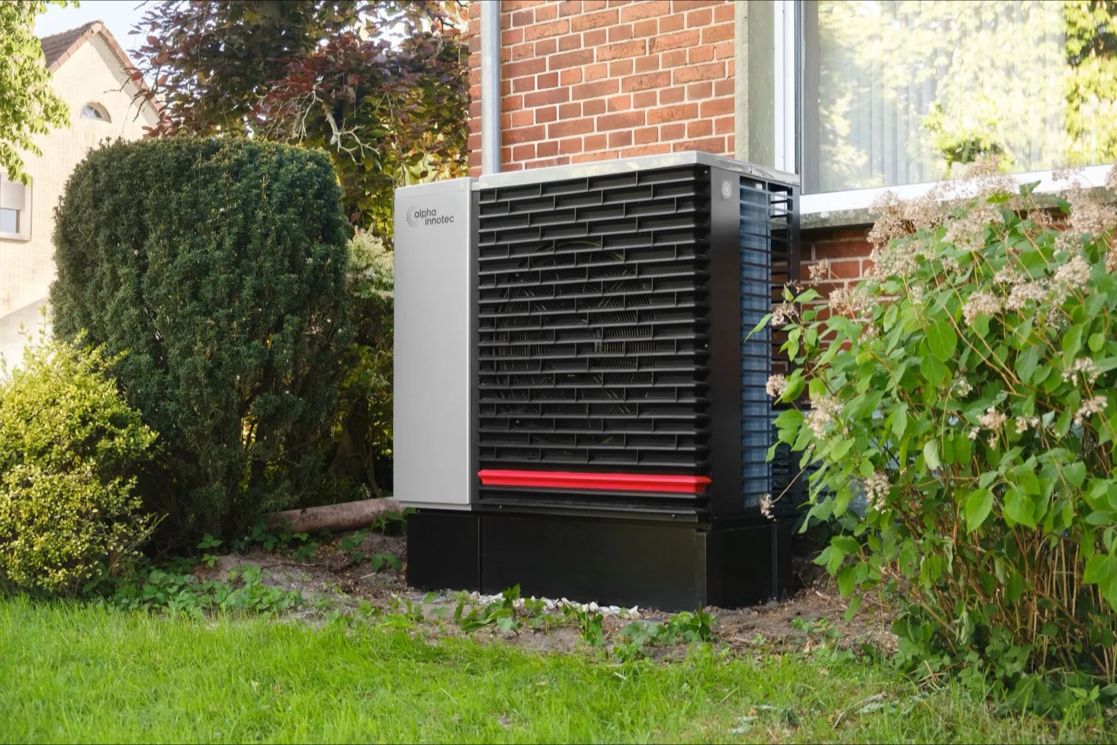 Außeneinheit einer Luft-Wärmepumpe neben einem Wohnhaus im Garten